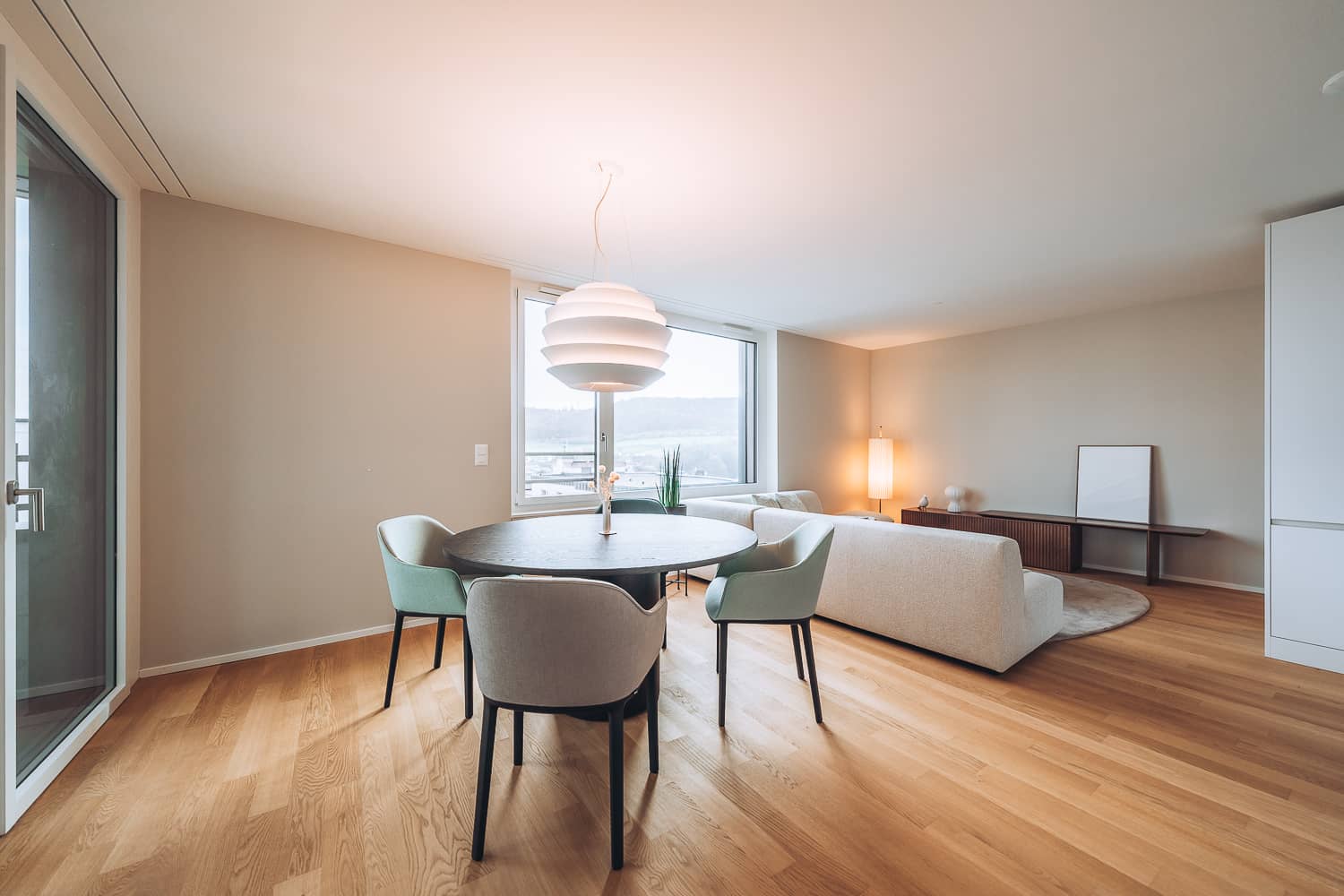 In einer grossen hellen Wohnung steht ein runder Esstisch mit Armlehnst&uuml;hlen rund herum